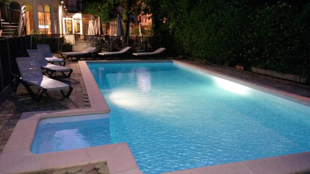 a swimming pool at night with chairs and tables at Hôtel Au Pavillon du Frêne in Lacaune