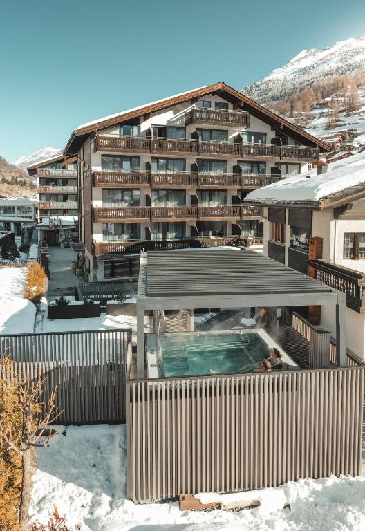 ツェルマットにあるAlpen Resort & Spaの雪中のスイミングプール付きの大きな建物