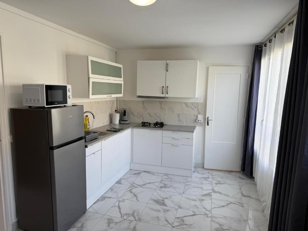 a kitchen with white cabinets and a black refrigerator at Carnot - VILLIERS LE BEL proche Aéroport ROISSY CHARLES DE GAULLES & PARIS in Villiers-le-Bel