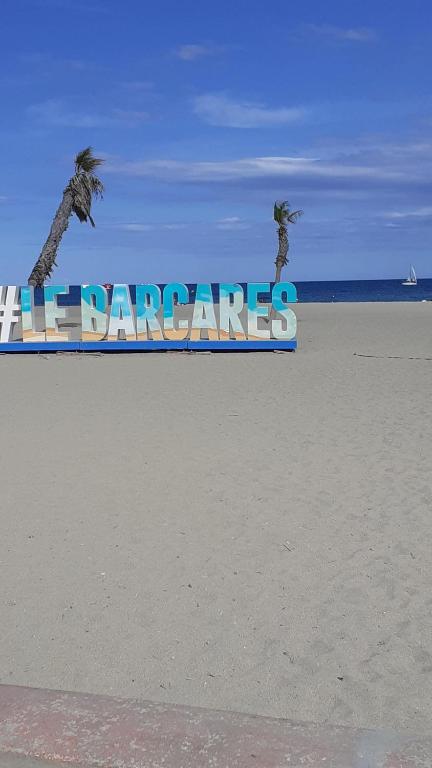 un panneau sur la plage avec deux palmiers dans l'établissement T2 50m PLAGE BARCARES PORT RDC, au Barcarès