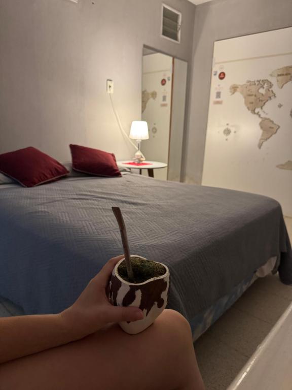 a person holding a cup with a plant in it next to a bed at La casita de la viña in Tinogasta