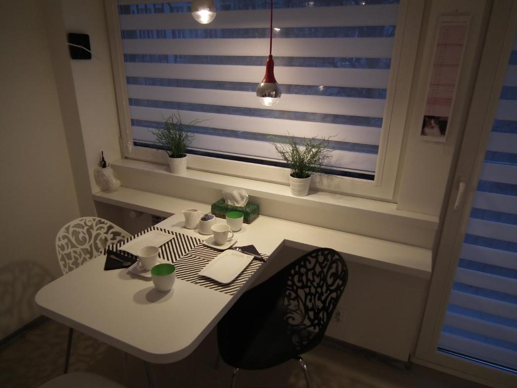 une table blanche avec des chaises et une fenêtre avec des plantes dans l'établissement Kazimir Apartament Lodz, à Łódź