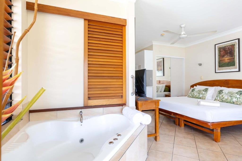 a bathroom with a bath tub and a bed at Honeymoon Spa Suite 53 in Port Douglas