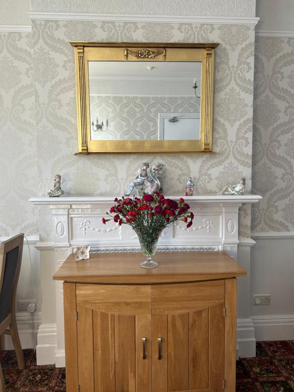 a vase of flowers on a wooden cabinet with a mirror at The Sandrock in Clacton-on-Sea