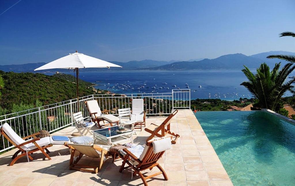 a swimming pool with chairs and an umbrella and the ocean at Villa Gardelina in Campomoro