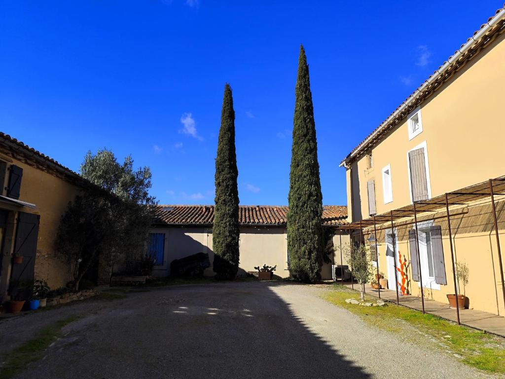une rue avec deux arbres devant un bâtiment dans l'établissement Les Grands Cyprès - chambres d'hôtes, à Conques-sur-Orbiel