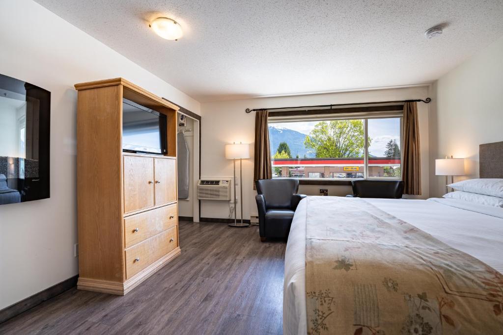 a hotel room with a bed and a desk and a window at Swiss Chalet Motel in Revelstoke