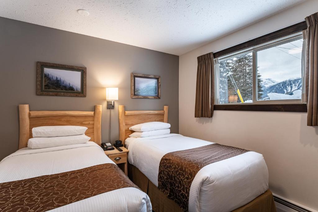 two beds in a hotel room with a window at Swiss Chalet Motel in Revelstoke