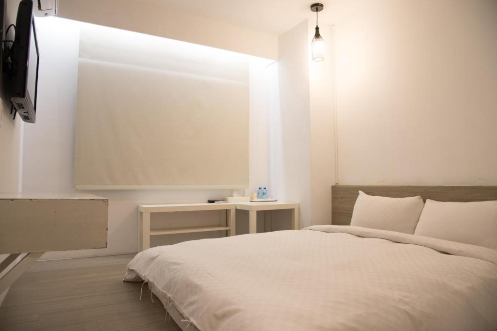 a white bedroom with a bed and a tv at Haogong Hotel in Taichung