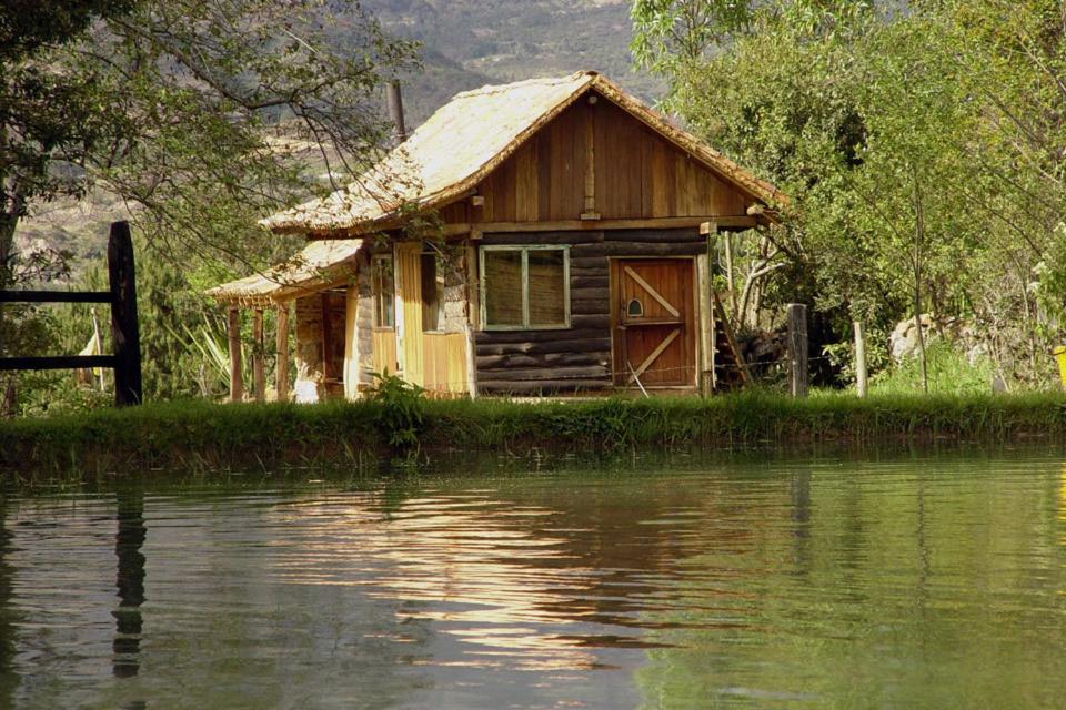 una pequeña casa junto a un cuerpo de agua en Hotel Ráquira Silvestre Lodge, en Tinjacá