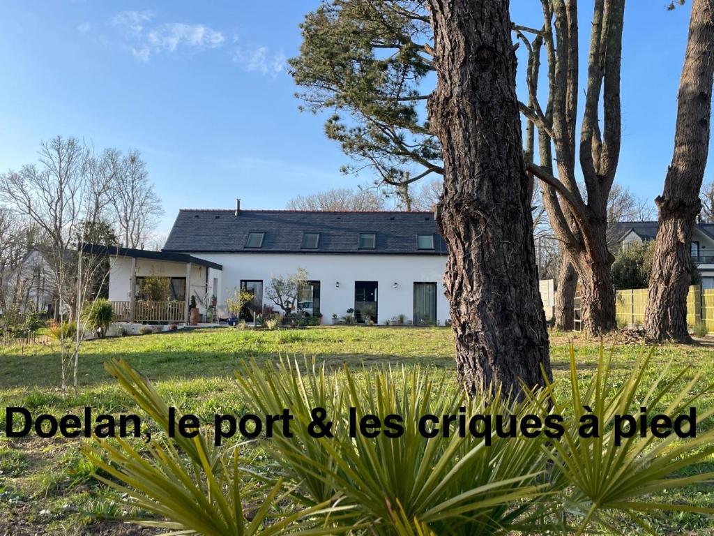 une maison blanche avec un arbre et les mots dolahu le port moins dans l'établissement Ty Glazu Villa neuve grand confort, jardin 1600m2, GR34, criques, restos et port Doelan à pied, à Clohars-Carnoët
