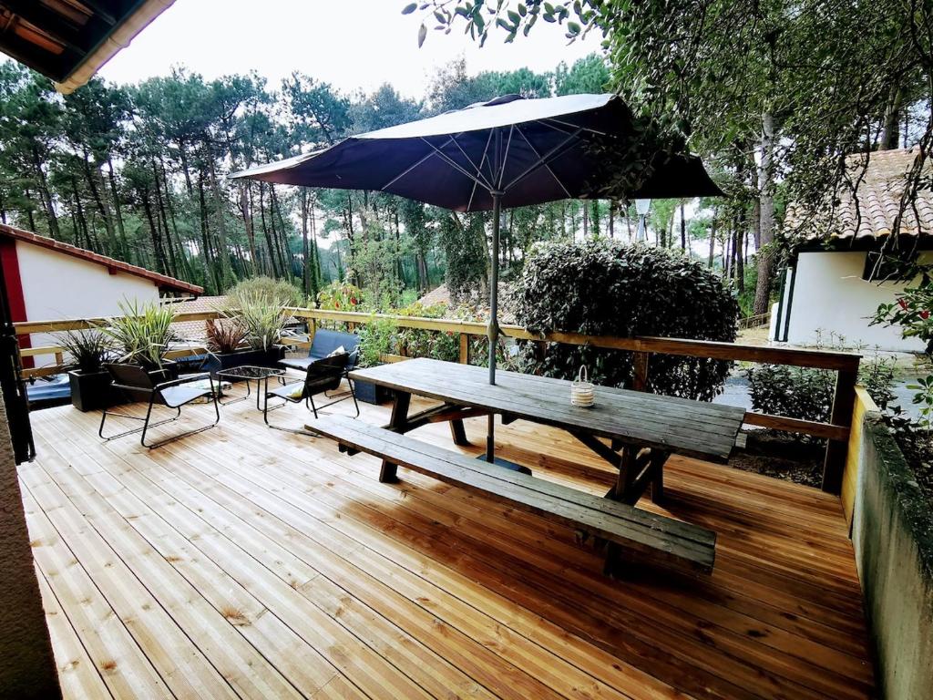 une terrasse en bois avec une table de pique-nique et un parasol dans l'établissement Uhaina, Maison proche Golf et Plage, à Moliets-et-Maa