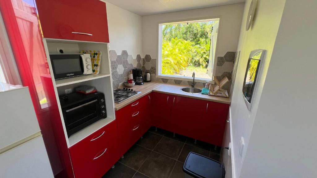 una piccola cucina con armadi rossi e una finestra di Bungalow LEWOZETAJ a Sainte-Anne