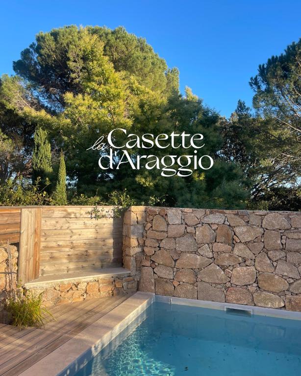 une piscine avec un mur en pierre et un panneau dans l'établissement Locations de La Casette d'Araggio, à Porto-Vecchio