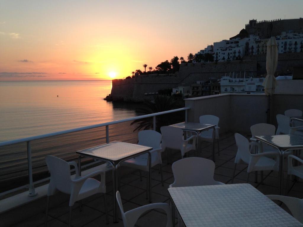 a balcony with tables and chairs and a sunset at Hotel Mare Nostrum in Peniscola