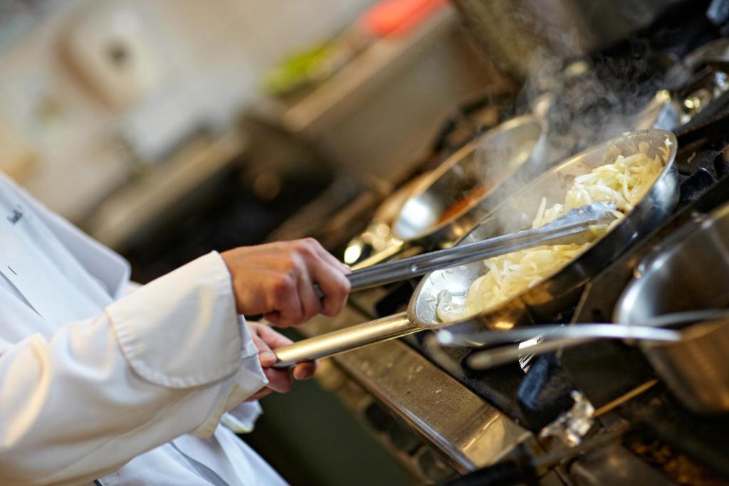 a chef is cooking food in a stove at Hotel Mazurkas in Ożarów Mazowiecki
