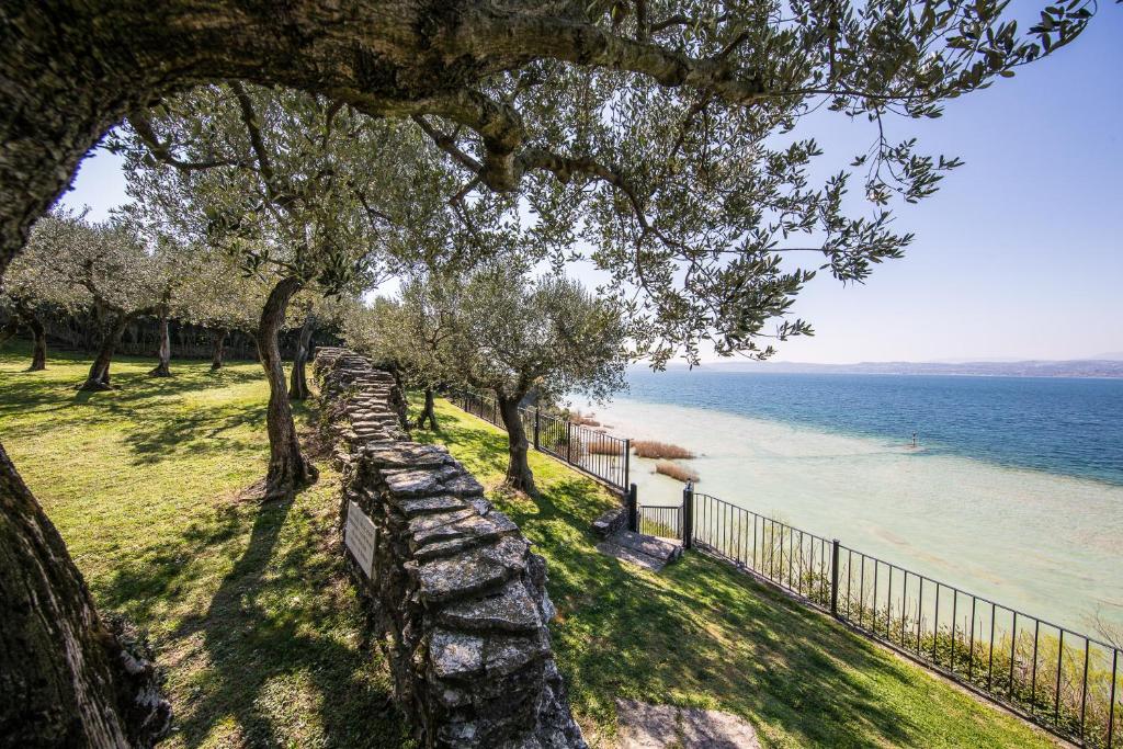 a stone wall next to the water with trees at Appartamento Ideal in Sirmione