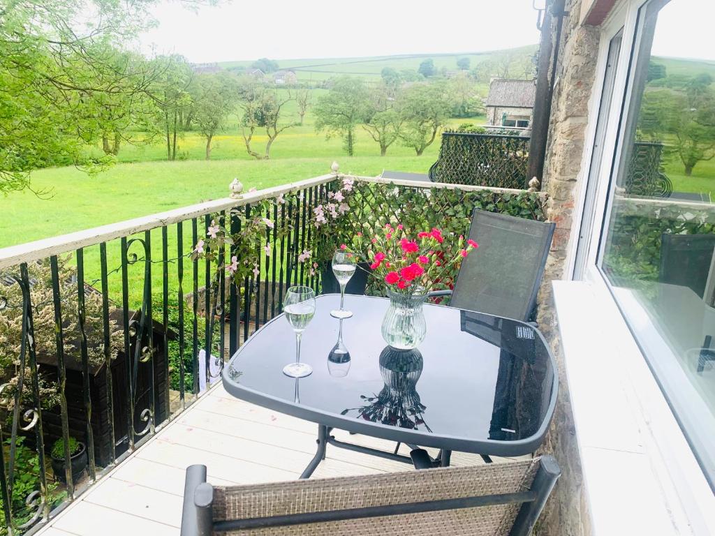 a glass table with wine glasses and flowers on a balcony at Tilly Cottage - overlooking Pendle Hill in Barrowford