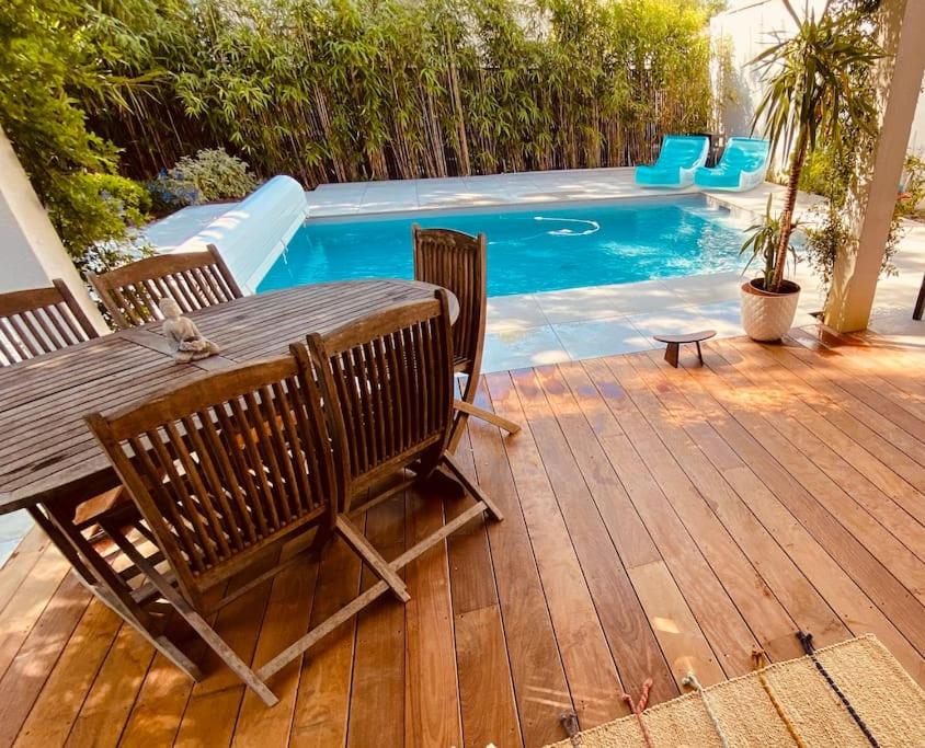 - une terrasse en bois avec une table et des chaises à côté de la piscine dans l'établissement Villa Poujeau - Piscine chauffée, à Le Pian-Médoc