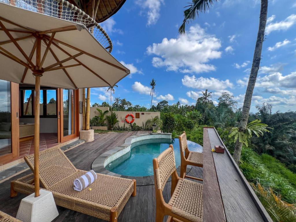 a villa with a pool and a deck with chairs and an umbrella at The Scape Valley Villas in Tampaksiring