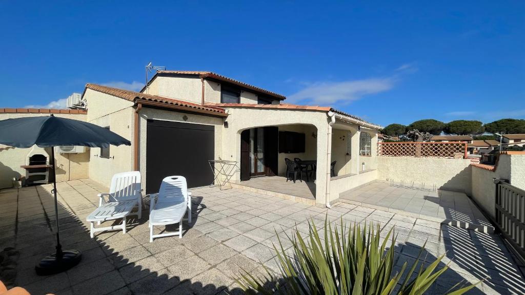 - une terrasse avec 2 chaises blanches et un parasol dans l'établissement Belle villa d'angle climatisée, residence TAMARIS, wifi, 2 chambres 4 couchages PORTIRAGNES PLAGE LRTAMM1, à Portiragnes