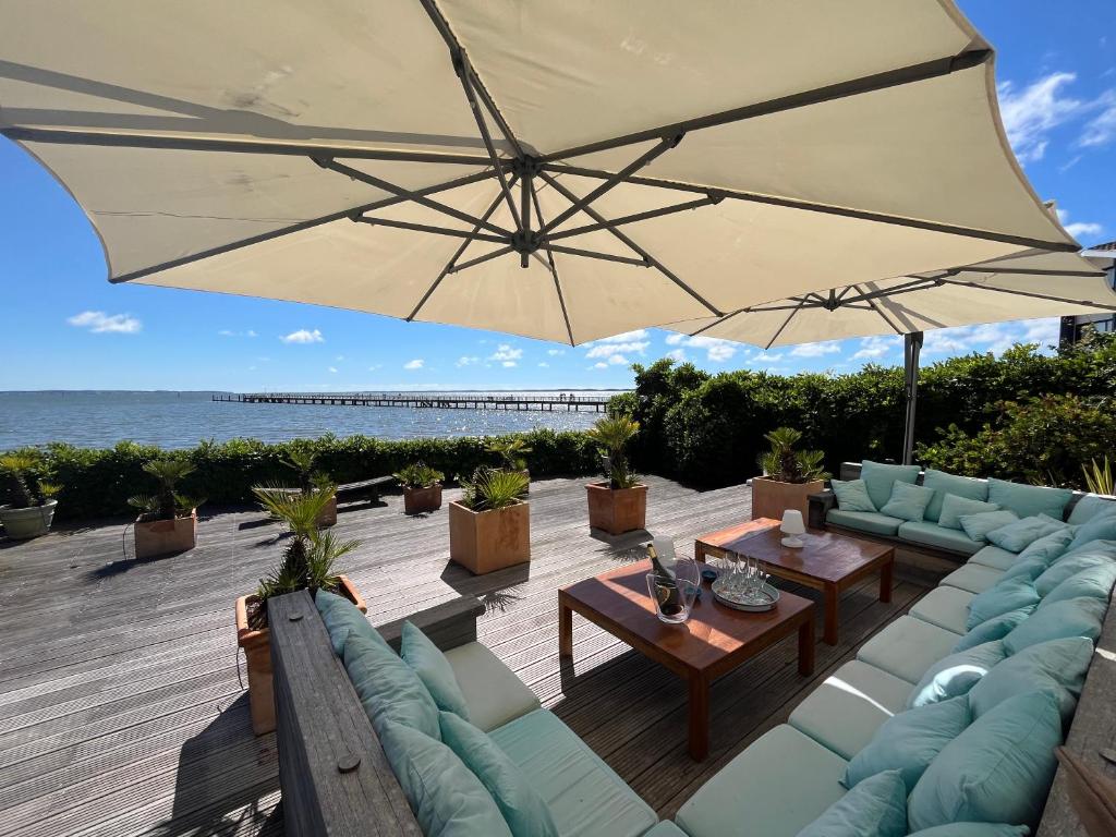 une terrasse avec des canapés et un parasol et l'océan dans l'établissement La Villa Cissia , sur la plage, à Andernos-les-Bains