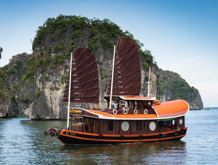 an orange boat in the water next to an island at Halong Ocean Cruise 6 in Ðảo Cát Bà