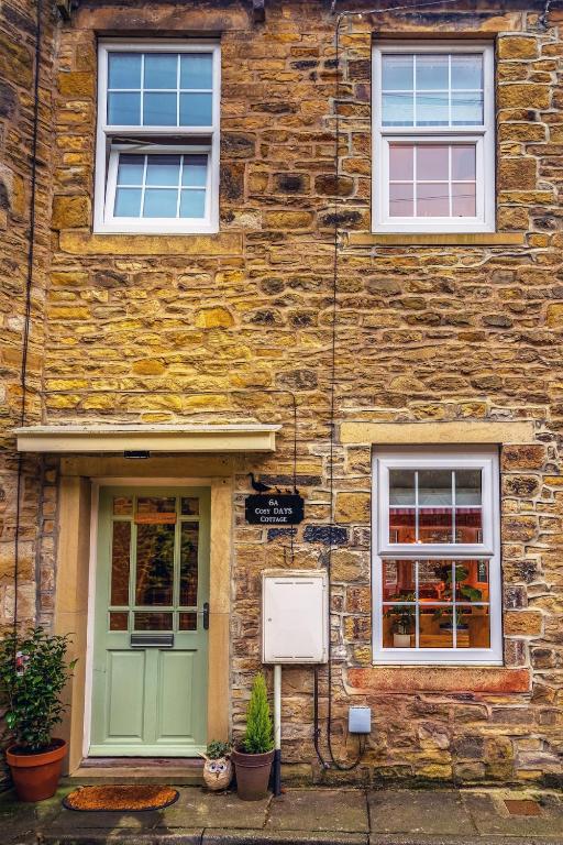 a stone building with a green door and two windows at Cosy Days Cottage in Skipton