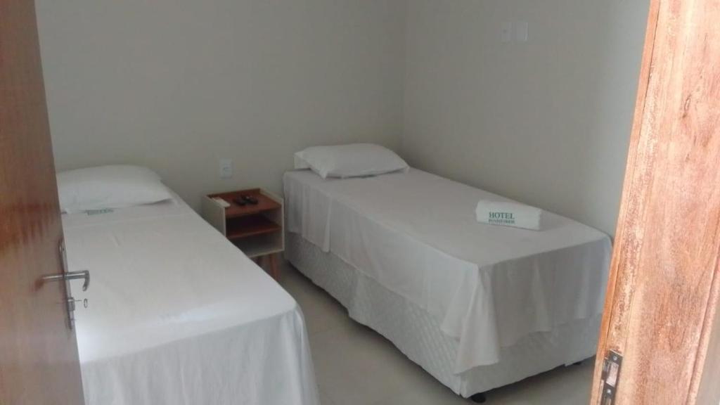 two beds in a small room with white sheets at Hotel Pinheiros in Nossa Senhora da Glória