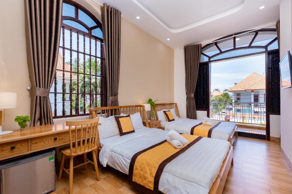 two beds in a room with a desk and windows at Hoàng My Villa Bãi Sau Vũng Tàu in Vung Tau