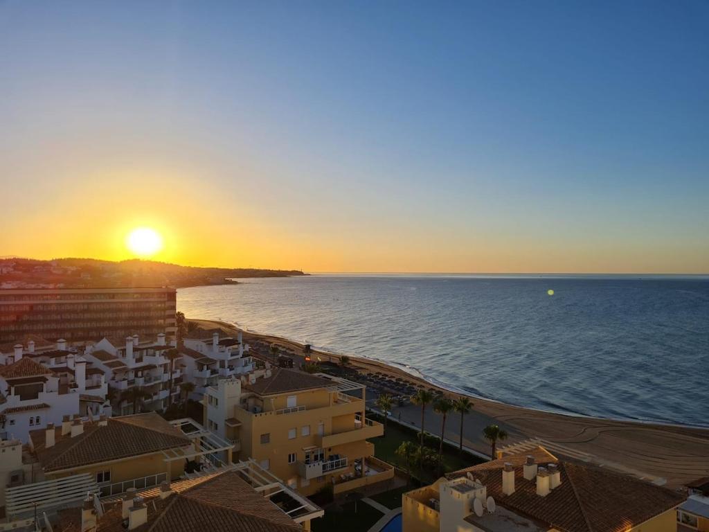 Una puesta de sol sobre una playa con edificios y el océano. en Beach Front La Cala Penthouse studio Apartment, en La Cala de Mijas