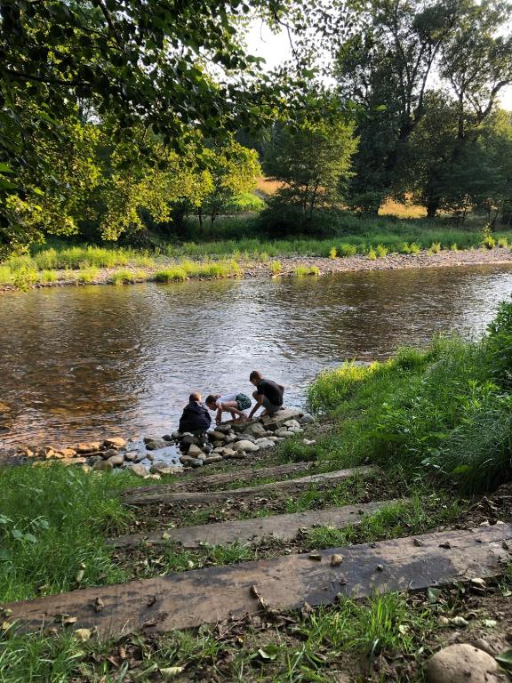 three people sitting on rocks by a river at Camping Les Berges Du Doux in Colombier-le-Vieux