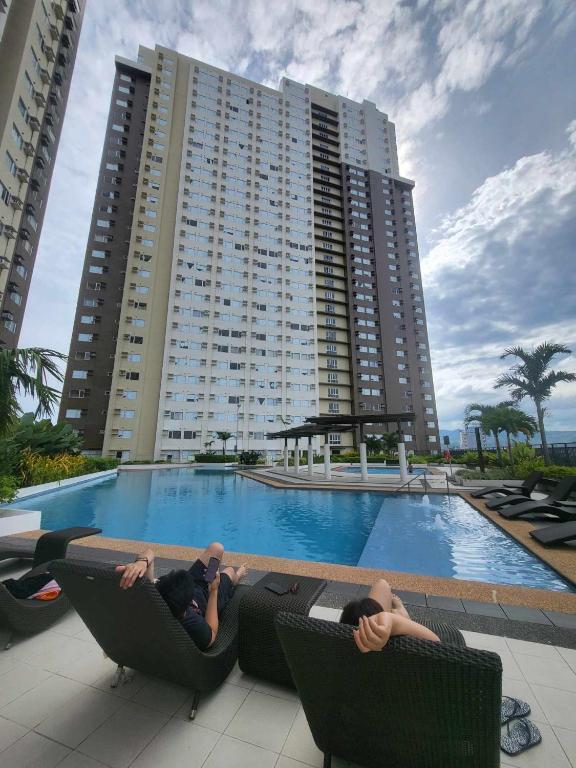 two people laying in chairs in front of a large building at Cozy City Escape - Avida Aspira Tower 1, CDO in Cagayan de Oro