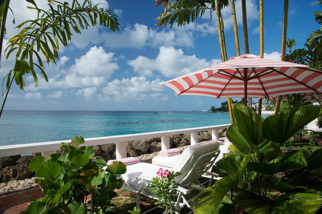 a balcony with chairs and an umbrella and the ocean at Cobblers Cove - Barbados in Saint Peter