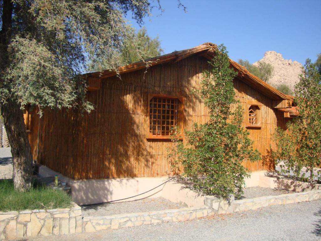 una casa de madera con un árbol delante en Noor Majan Camp, en Bilād Manaḩ