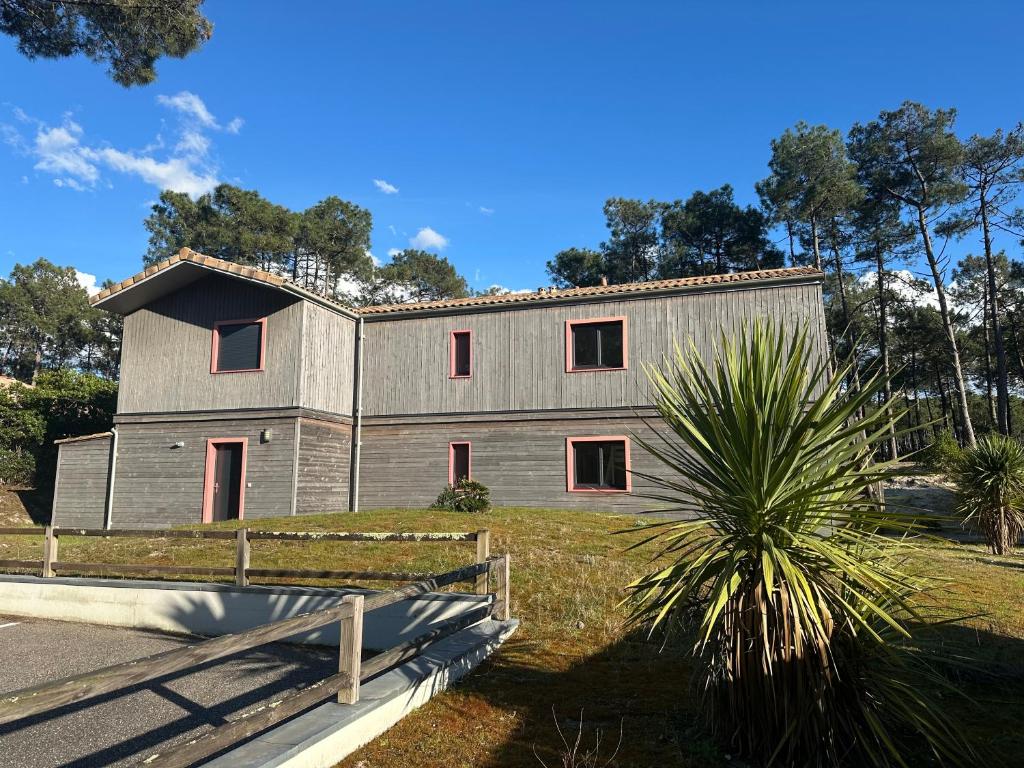 a gray building with red windows and a palm tree at Villa Orchidee in Lacanau-Océan