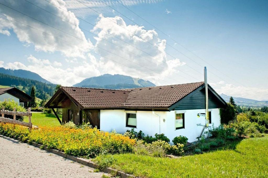 a white house with a brown roof in a field at Ferienhaus Gamssteige im Feriendorf Reichenbach G21 in Nesselwang