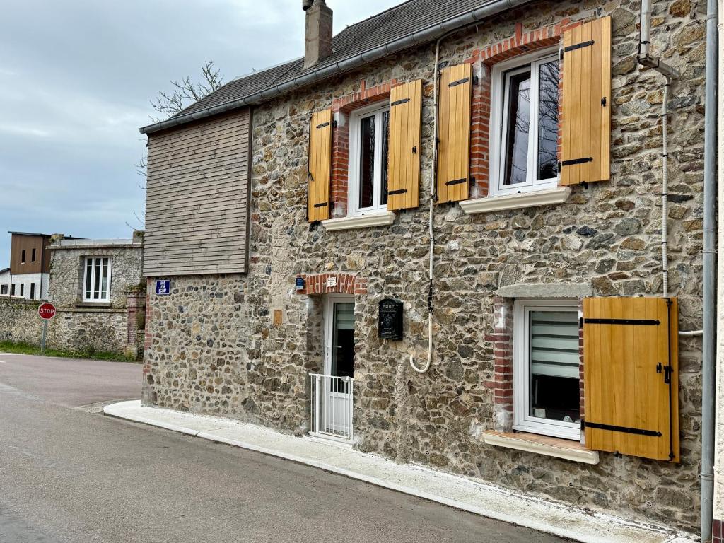 a stone building with wooden shutters on a street at Petite maison Normande Calme Meublé Tourisme 2 étoiles in Agon Coutainville