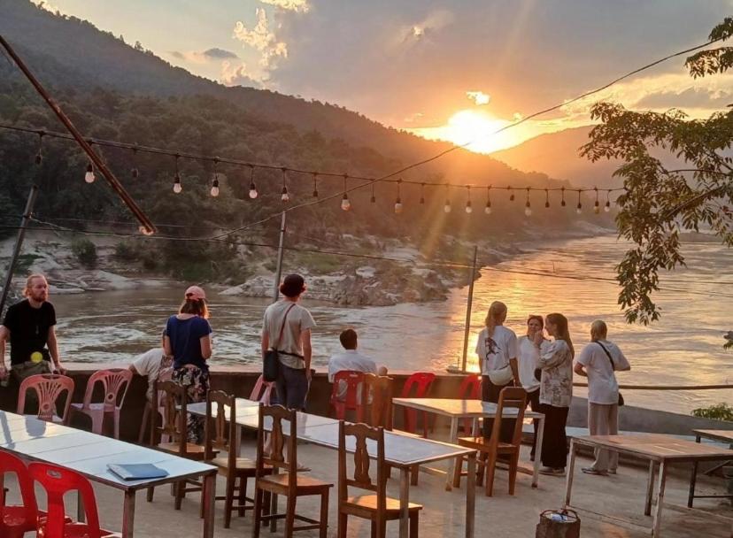 a group of people standing at tables near a river at MEKONG BACKPACKERS Pakbeng in Pakbeng