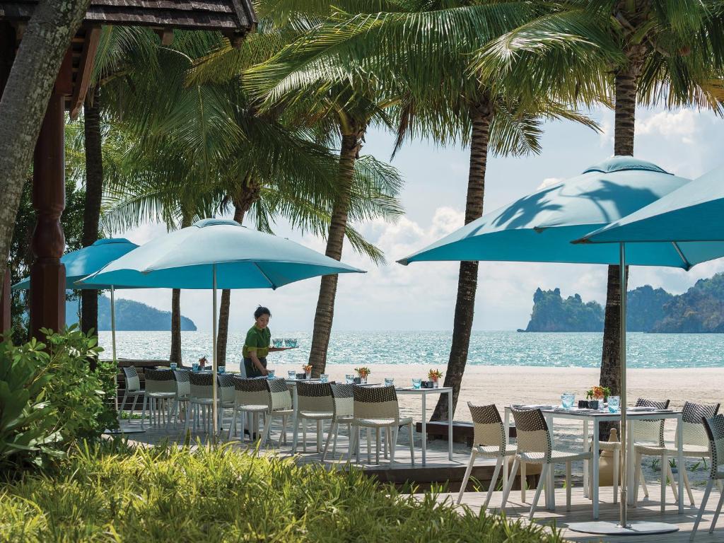 a table and chairs with blue umbrellas on the beach at Four Seasons Resort Langkawi in Tanjung Rhu