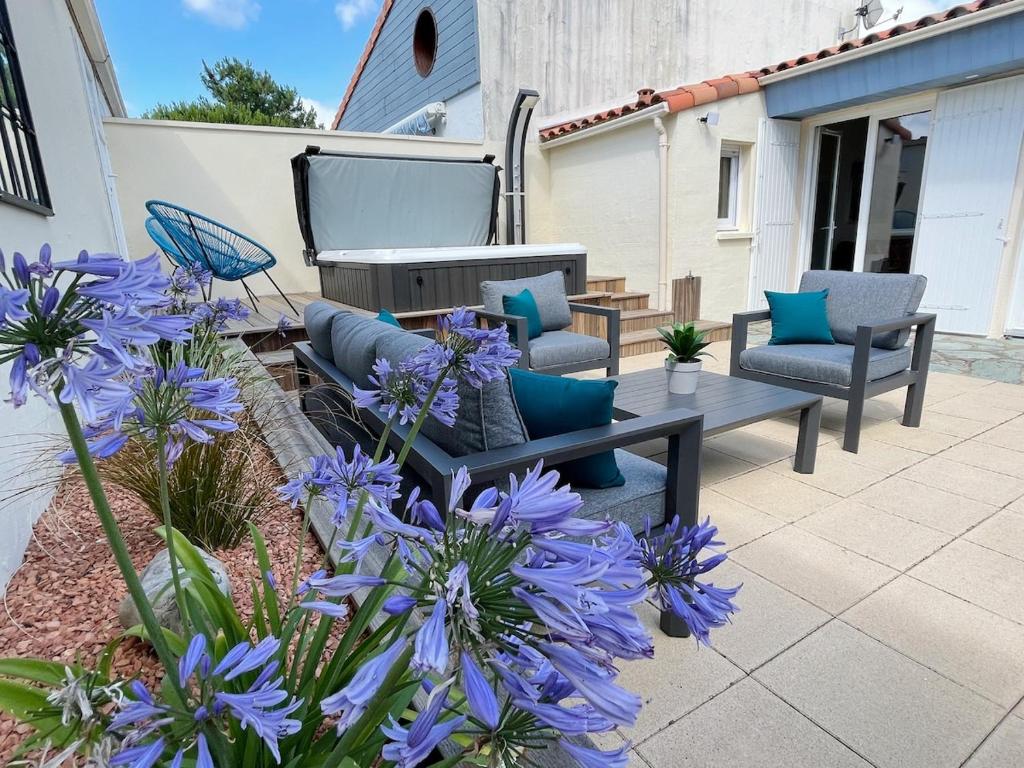 eine Terrasse mit Stühlen und einem Tisch und lila Blumen in der Unterkunft Le Rivage, maison proche mer avec Spa in Les Sables-dʼOlonne