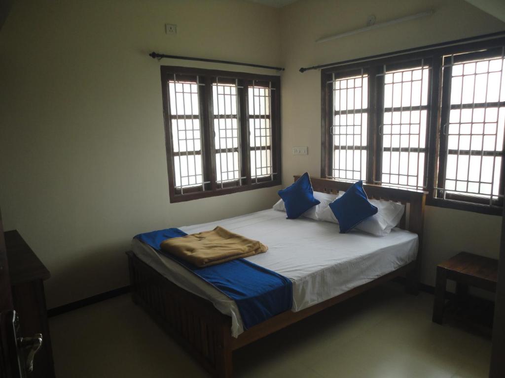 a bedroom with a bed with blue pillows and windows at Sanvika Hotels & Service Apartments in Coimbatore