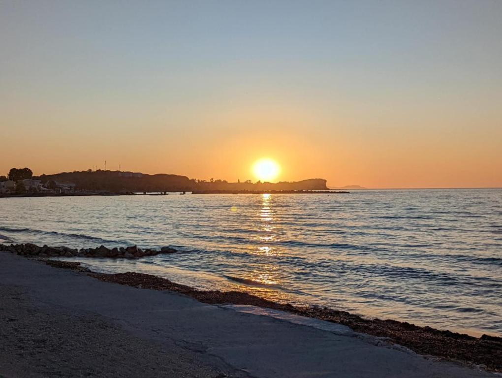 a sunset on a beach with the sun setting at Dolphin Apt & Studios -Near the Beach in Roda