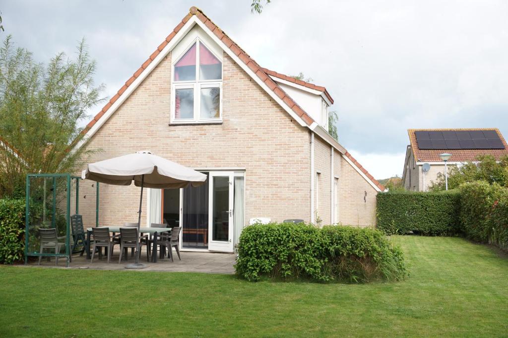 a house with a table and an umbrella in the yard at Kustverhuur, Park Scheldeveste Zwin 015, met grote omheinde tuin in Breskens