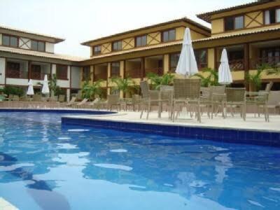 a hotel with a swimming pool with chairs and umbrellas at Enseada Praia do Forte in Praia do Forte