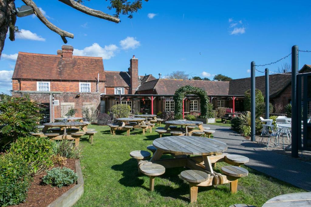 un jardín con mesas y bancos frente a un edificio en The Huntsman of Brockenhurst en Brockenhurst