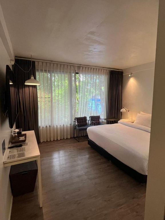 A bright double room with a large bed, desk, lounge chairs and a full-height window.
