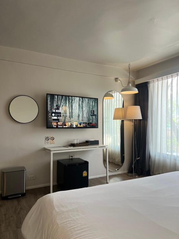 A bedroom view with a wall-mounted TV, minibar, desk and bright curtained window.