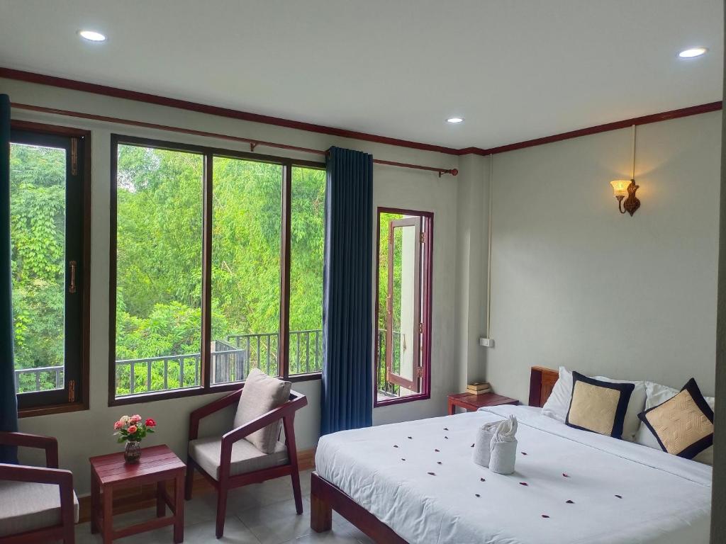a bedroom with a bed and two chairs and windows at Dok Champa Resort in Vang Vieng