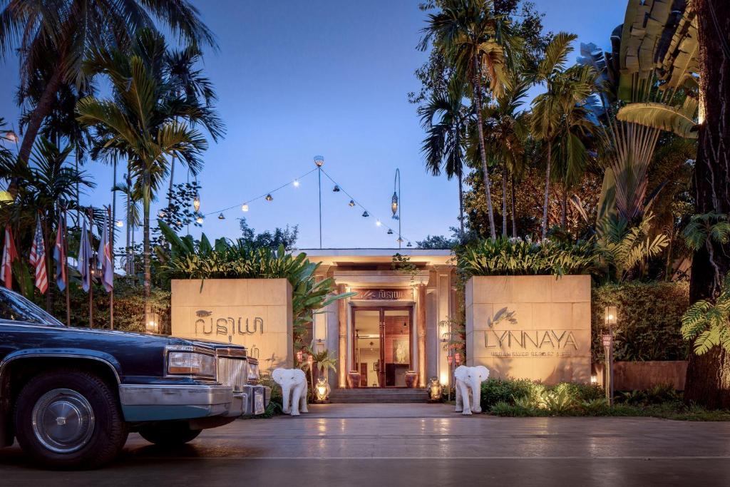 a car parked in front of a building with palm trees at Lynnaya Urban River Resort in Siem Reap